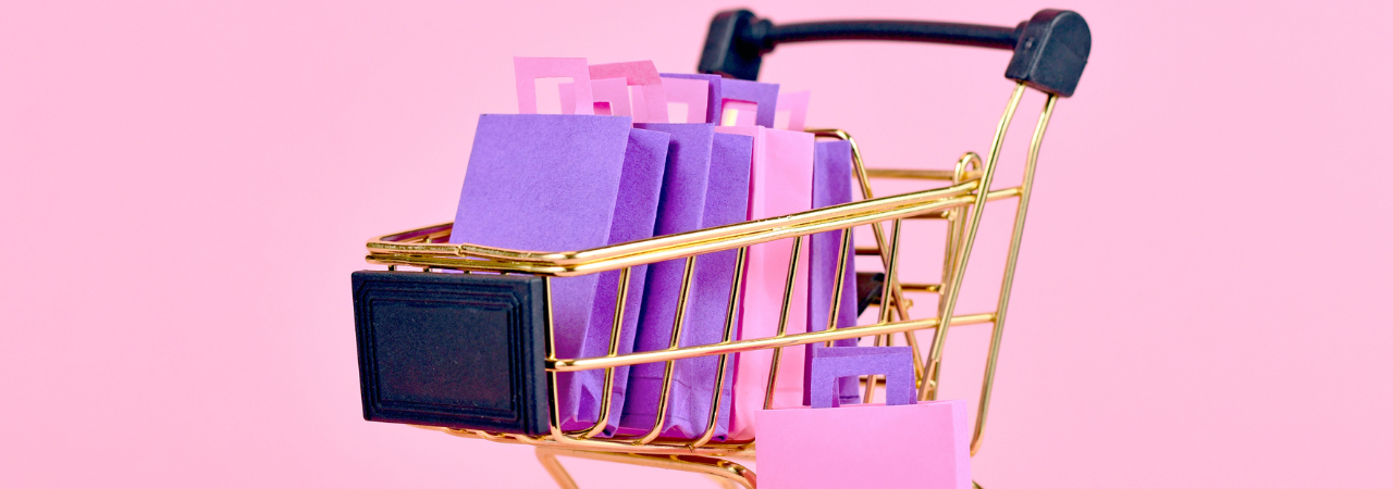 Pink background with small gold trolley and paper shopping bags inside