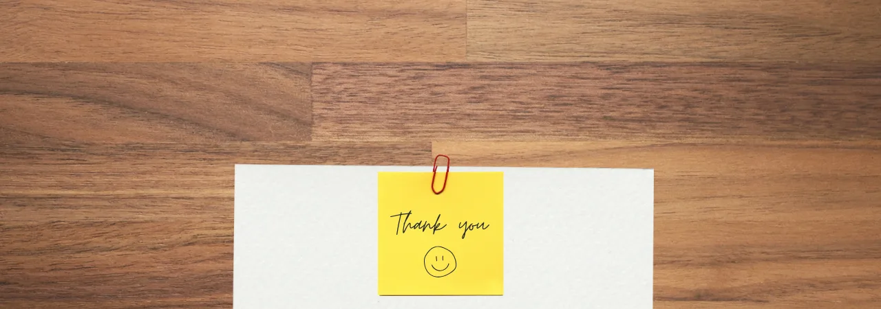 piece of paper on desk with post it noted saying 'thank you', with a smiley face on it