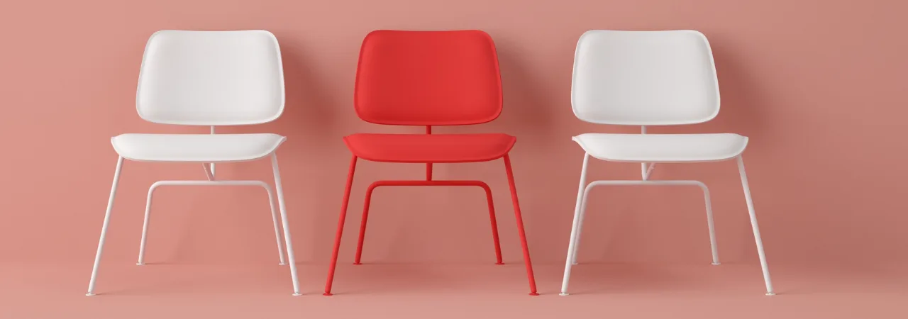 red chair between two white chairs, lined up against a wall