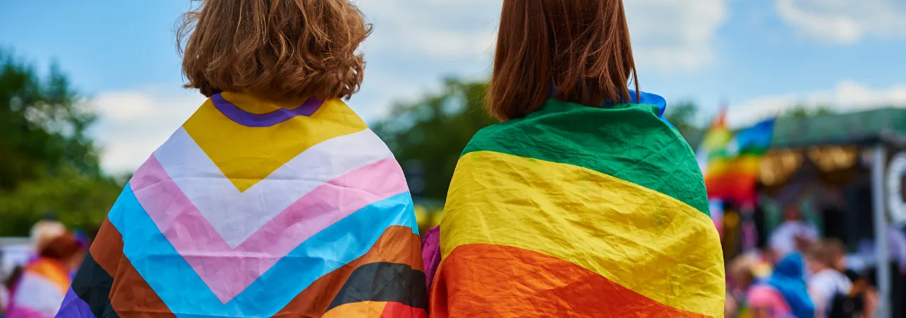 two people looking out at park, wearing pride flags