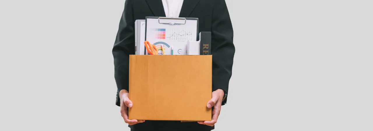 A man in a suit holding a moving box infront of a grey background